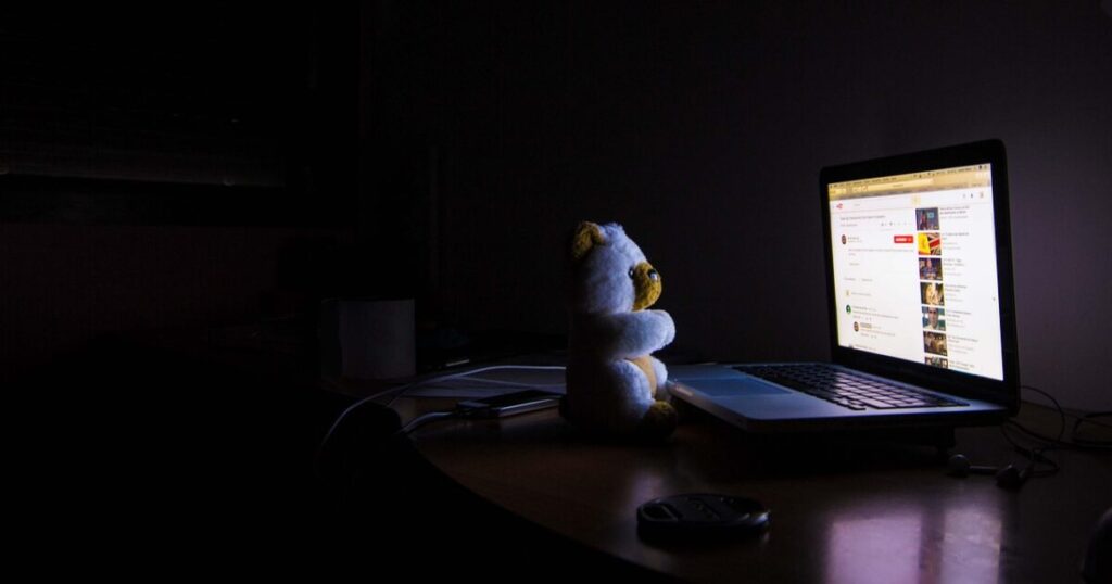 暗い部屋でノートパソコンの前に座るぬいぐるみ