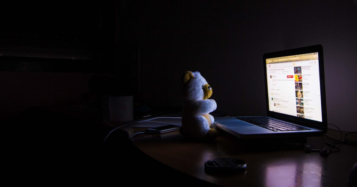 暗い部屋でノートパソコンの前に座るぬいぐるみ
