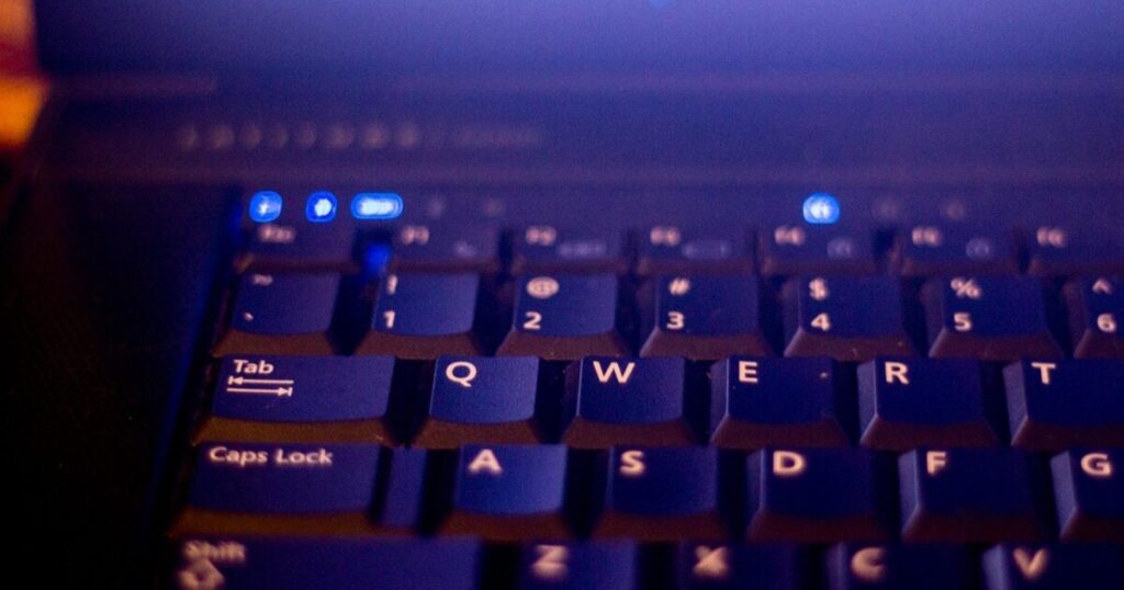 青いインジケーターが光るノートパソコンのキーボードクローズアップ