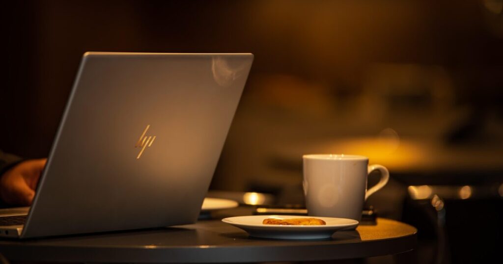 カフェのテーブルに置かれたHPノートパソコンとコーヒーカップとクッキー